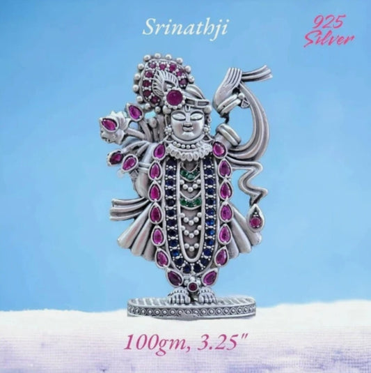 Pure silver Srinathji murti adorned with detailed ruby and emerald stones on blue background
